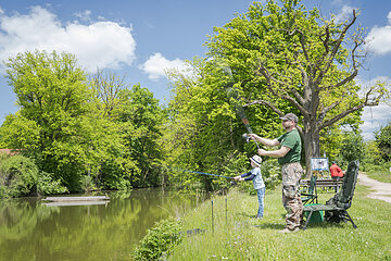 Vater und Sohn angeln am Karlsgraben. Vater steht und holt den Fisch aus dem Gewässer.