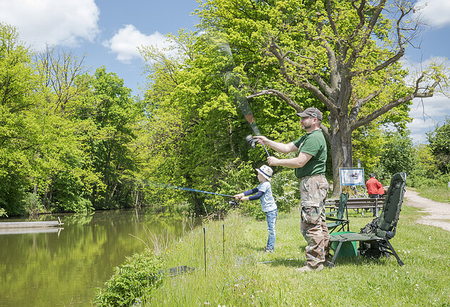 Vater und Sohn angeln am Karlsgraben. Vater steht und holt den Fisch aus dem Gewässer.