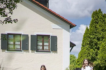 Zwei Mädchen führen Ponys vor einem Haus auf dem Weg.
