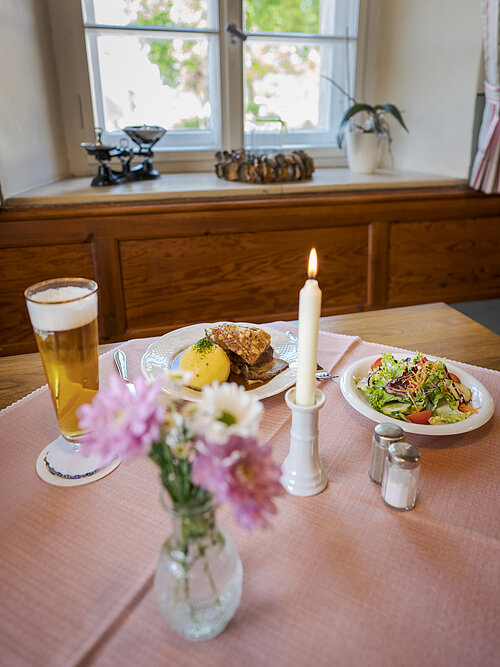 Gaststube ohne Personen, gedeckter Tisch mit Weizen, Schäufele, Kloß und Salat