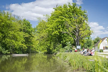 Familie sitzt mit Blick auf dem Karlsgraben. In der Mitte sieht man ein Kanu schwimmen.