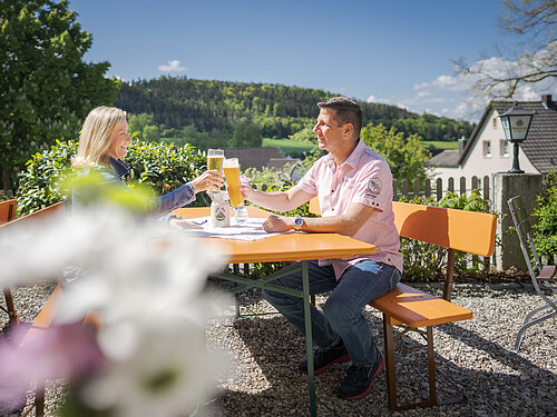 Biergarten, Pärchen prostet sich zu, Fernblick, unscharfe Blume im Vordergrund