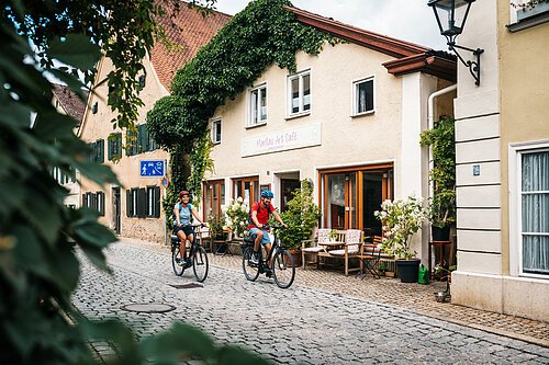 Zwei Radler mit blauem und rotem Shirt fahren durch die Altstadt Pappenheims.