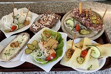 Auf einem Tablett sind verschiedene Brotzeiten wie Butterbrot, Wurstsalat, Käsebrot, Schinkenbrot, Rettich und Tartarbrot zu sehen.