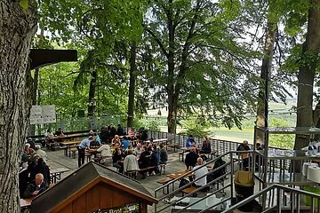 Von der oberen Terrasse hat man den Blick auf die untere, man sieht Gäste an den Tischen und einen Teil des großen, alten Baumbestandes