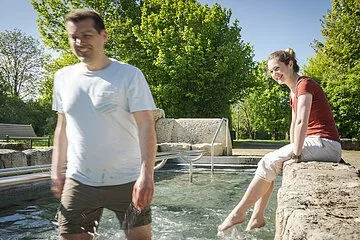 Pärchen beim Wassertreten im Kurpark wobei der Mann im Vordergrund steht.