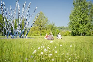Yoga in der Gruppe im Kurpark. Kunstwerk mit langen Stangen und Bäume sind im Bild Hauptakteur