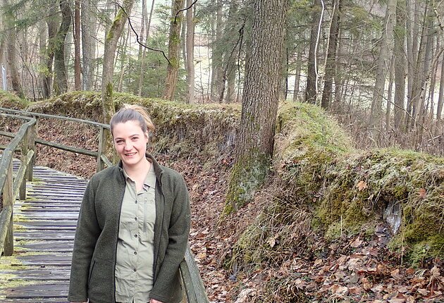 Die Naturpark-Rangerin Ann-Katrin Stockinger steht im Wald an einem Geländer neben der Steinernen Rinne