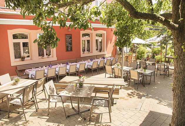 Lauschiger Biergarten unter Bäumen mit Sitzmöglichkeiten