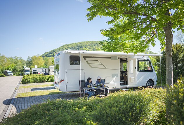 Pärchen sitzt vor dem Wohnmobil an einem Tisch und liest in der NPA-Zeitung