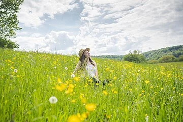 Blumenwiese am Burgstall, mittendrin sitzend Person weiblich mit Hut.