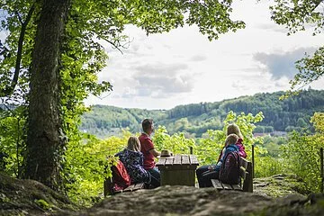 Familie rastet unter Bäumen bei strahlenden Sonnenschein und genießen den Ausblick.