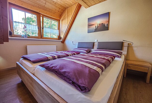 Ein gemütliches Doppelbett unter dem Dachgiebel mit lila Bettwäsche