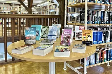 Auf einem Tisch liegen mehrere Bücher aus, im Hintergrund die Bücherregale