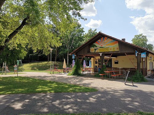Ein Gebäude mit überdachten Sitzmöglichkeiten, daneben der Spielplatz an der Denkmalslok