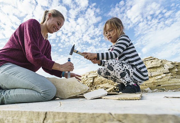 Eine Frau mit Kind lösen vorsichtig Gesteinsplatten mit Hammer und Meißel, auf der Suche nach Fossilienversteinerung.