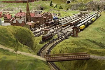 Eine Miniaturlandschaft umgeben von grün. Eisenbahnschienen und ein Dorf.