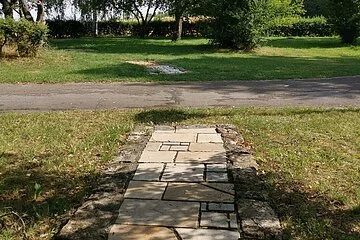 Ein Element des Barfußpfades im Kurpark mit gepflasterten Jura-Natur-Steinen, anschließend folgt ein geteerter Weg und die nächste Abteilung.