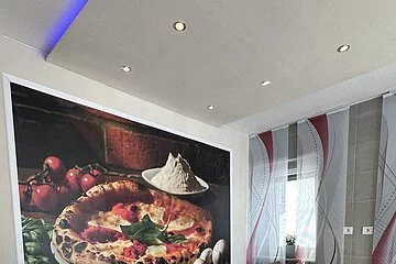 Sitzmöglichkeiten in der Pizzeria mit einem großen Wandbild, auf dem eine Pizza abgebildet ist