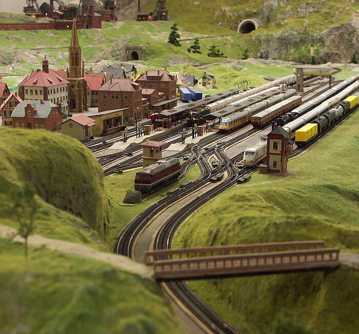 Eine Miniaturlandschaft umgeben von grün. Eisenbahnschienen und ein Dorf.