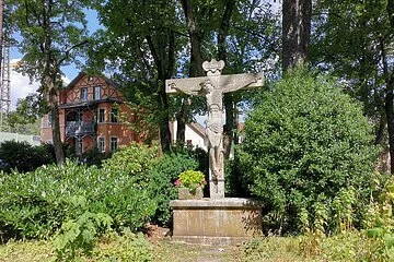 Ein Steinkreuz umgeben von Büschen und hohen Bäumen im Stadtpark
