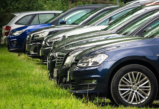 Mehrere Autos parken hintereinander, links eine Wiese