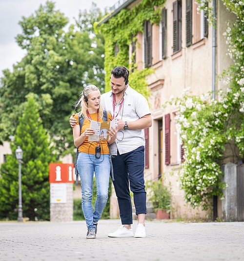 Zwei Touristen laufen entlang der Straße zwischen Museum und Stadtschloss Treuchtlingen. Sie lauschen der Stadttour über die Kopfhörer der Audioguides.