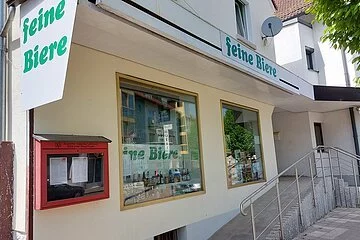 Der Eingang des Bierladens "Feine Biere mit barrierefreier Rollstuhl-Rampe. In der linken, oberen Ecke hängt eine weiße Fahne mit grüner Aufschrift.