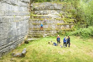 Frontaufnahme eines Kletterhangs des Steinbruchs bei Möhren. Eine Gruppe an Kletterern steht vor dem Hang.