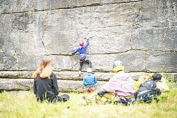 Frontaufnahme eines Kletterhangs am Steinbruch Möhren. Personen sitzen vor dem Hang und beobachten zwei professionelle Kletterer im Hintergrund.