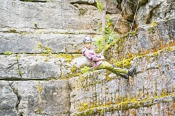 Aufnahme eines Hangs am Klettersteinbruch Möhren. Eine Kletterin seilt sich mit professioneller Ausrüstung von der Steinwand ab.
