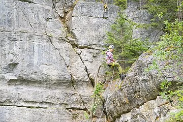 Aufnahme des Klettersteinbruchs bei Möhren. Eine Kletterin erklimmt die Steinwand, während sie von einer Person am Fuße gesichert wird.