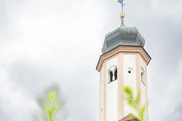 Seitenansicht der Lambertuskirche aus der Froschperspektive und bewölktem Himmel. Im Vordergrund befinden sich grüne Pflanzen.