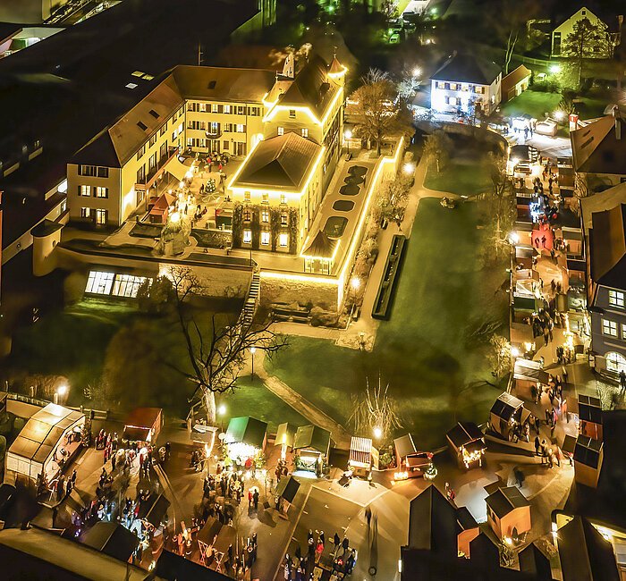 Der Weihnachtsmarkt um das hell erleuchtete Stadtschloss, um den Schlossgraben fügen sich die Holzhütten.