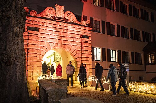 Rot beleuchteter Torbogen mit gold beleuchteter Brücke zum Stadtschloss.