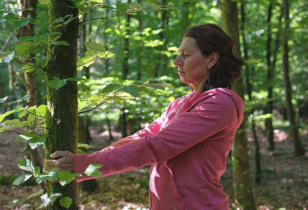 Eine Frau in pinker Jacke berührt einen Baumstamm