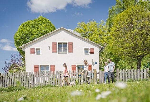 Familie verlässt den Garten eines kleines Hauses mit roten Fensterläden