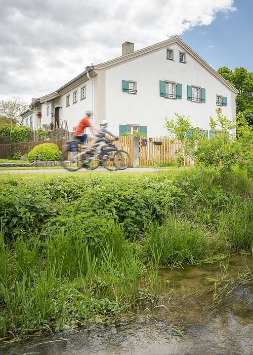 Zwei Radler fahren durch Wettelsheim am Bach entlang an Jurahäusern vorbei