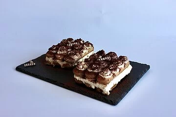 Zwei Portionen Tiramisu auf schwarzer Schieferplatte angerichtet.