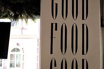 Blick auf die Straße durch das Schaufenster. Im Schaufenster steht ein Schild auf dem steht: good food, good mood