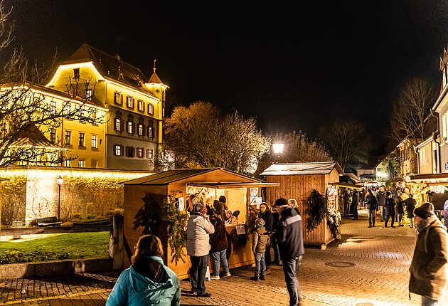 Im Vordergrund die romantisch beleuchtete Budengasse um den Schlossgraben mit Besuchern, im Hintergrund das beleuchtete Stadtschloss