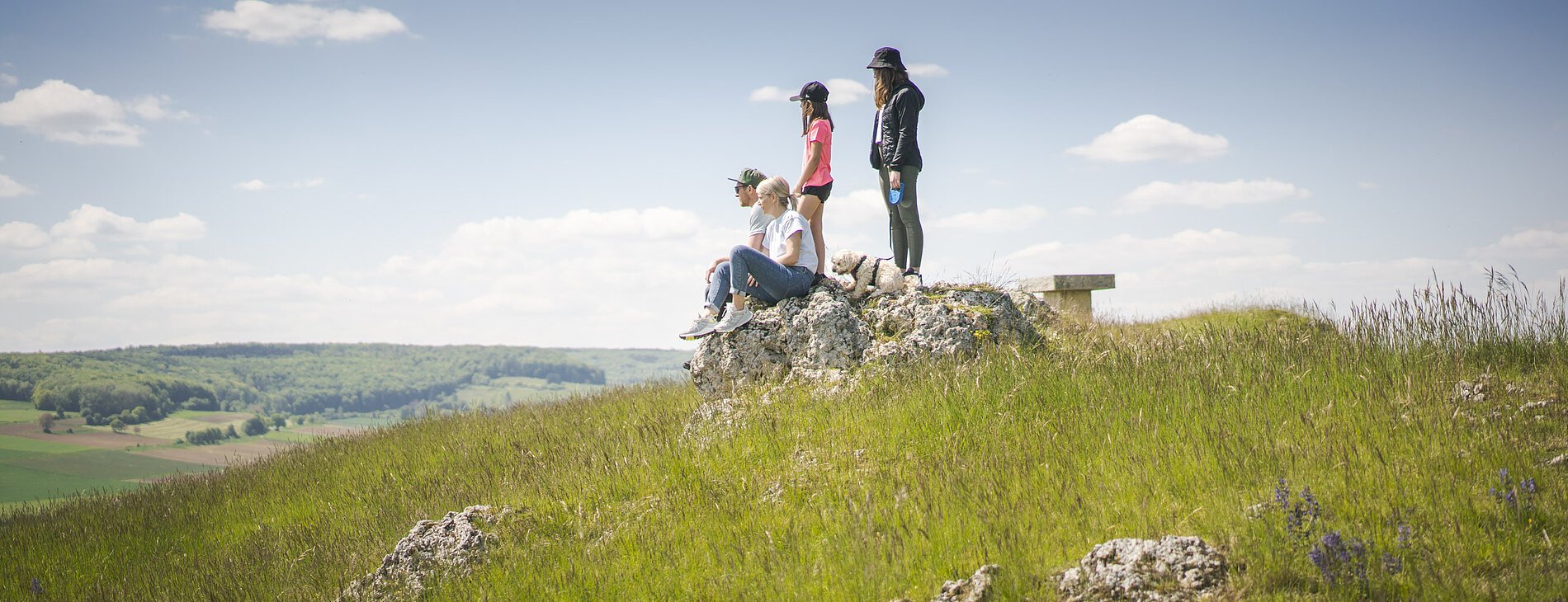 Familie mit Hund sitzen auf dem Bubenheimer Berg auf einem Felsen. Kinder stehen hinter den Eltern