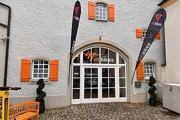 Ein graues Haus mit großer weißer Eingangstüre aus Glas, orangen-farbige Fensterläden