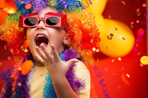Ein Kind mit roter Brille und bunter Perrücke und Konfetti im Hintergrund