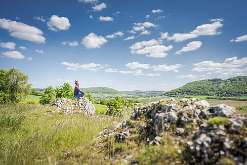 Frau sitzt auf einem Stein in Yogapose im Vordergrund ein Felsen