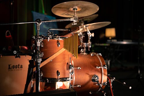 Ein Schlagzeug aus Holz mit Drums, Crash-Becken und Hi Hat, Percussion. Im Hintergrund ein schwarzer Vorhang.