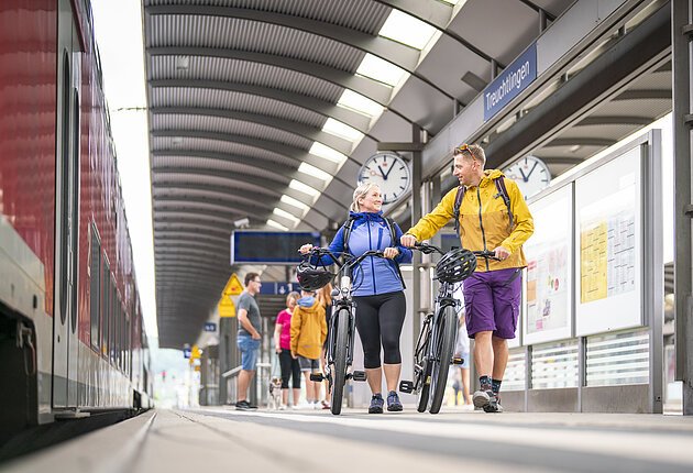 Aufnahme entlangeines Treuchtlinger Bahnsteigs. Im Hintergrund laufen einige Gäste entlang des Bahnsteigs. Ihnen voran ein Pärchen mit Ihren E-Bikes.