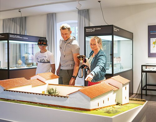 Eine Familie besucht die Abteilung der Abteilung Vor- und Frühgeschichte im Museum. Sie Blicken auf eine Nachbildung einer sogenannten Villa Rustica.