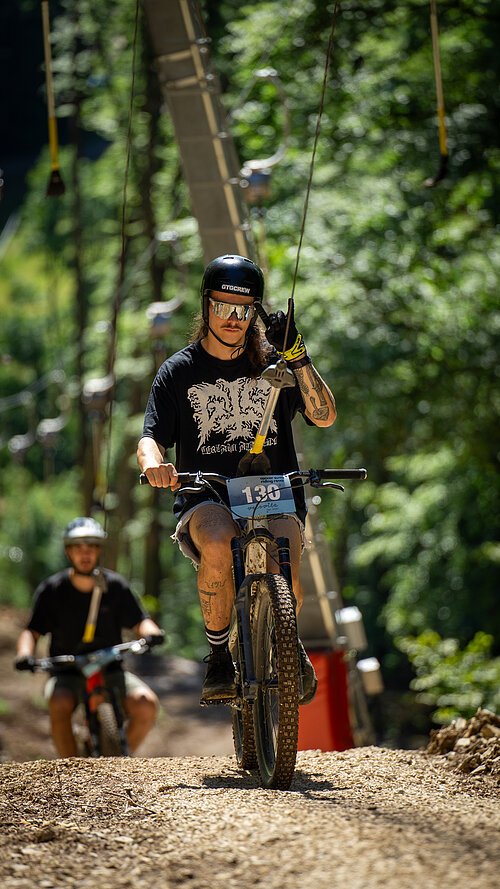 Auf dem Bild ist ein Mann mit einem Mountainbike zu sehen, welcher mit einem Bike-Lift hochgezogen werden.