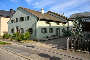 Jurahaus in Dettenheim, an der Hauptstraße gelegen, das Haus hat einen grünen Anstrich und Holzfensterläden, an der Stirnseite des Hauses befinden sich einige Sträucher